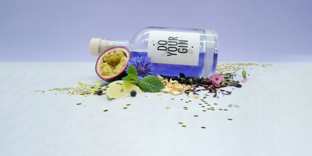 gin bottle with purple gin and flowers laying on passion fruit deco
